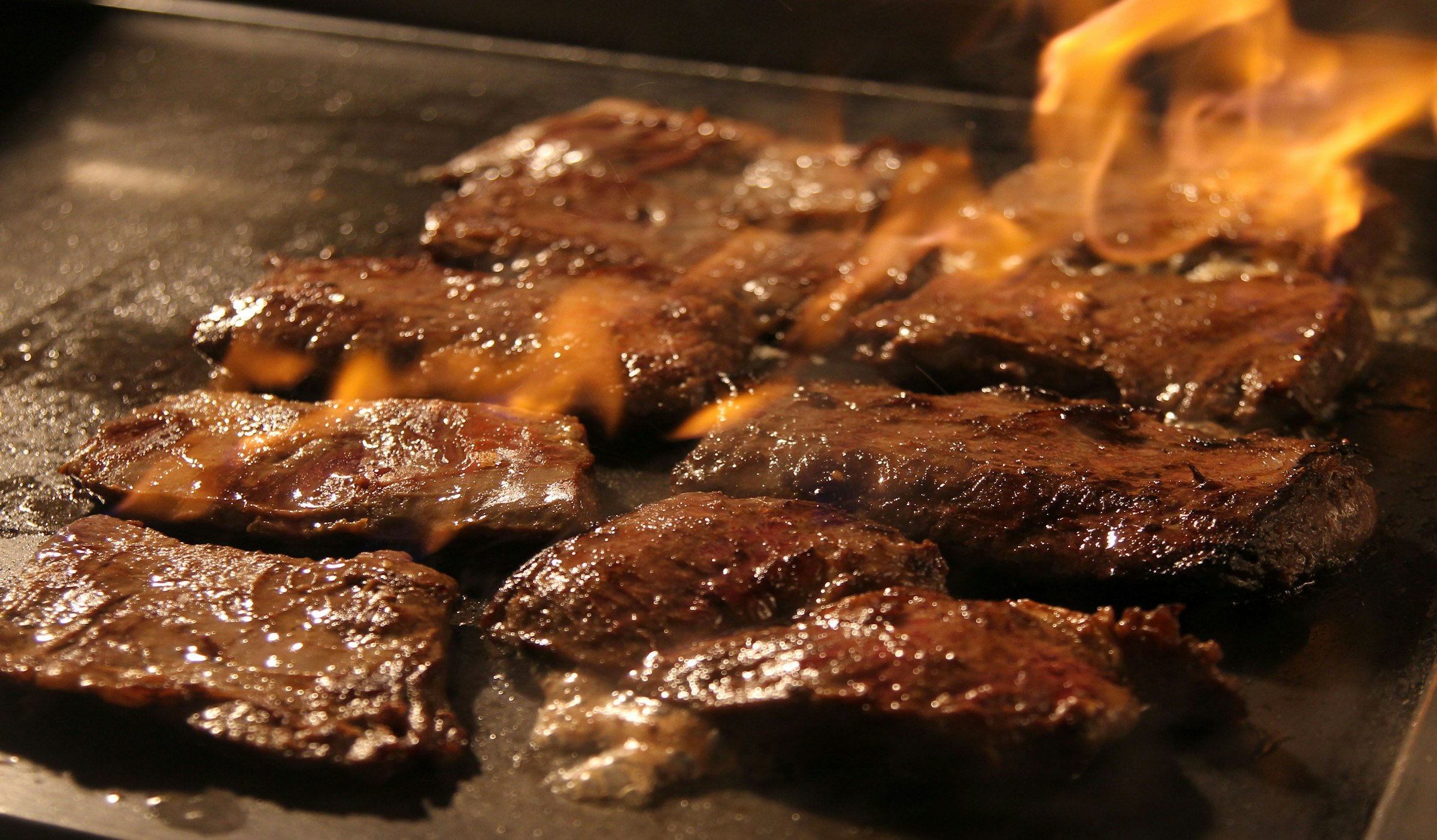 Steaks searing over open flame in the dark at Rooh's