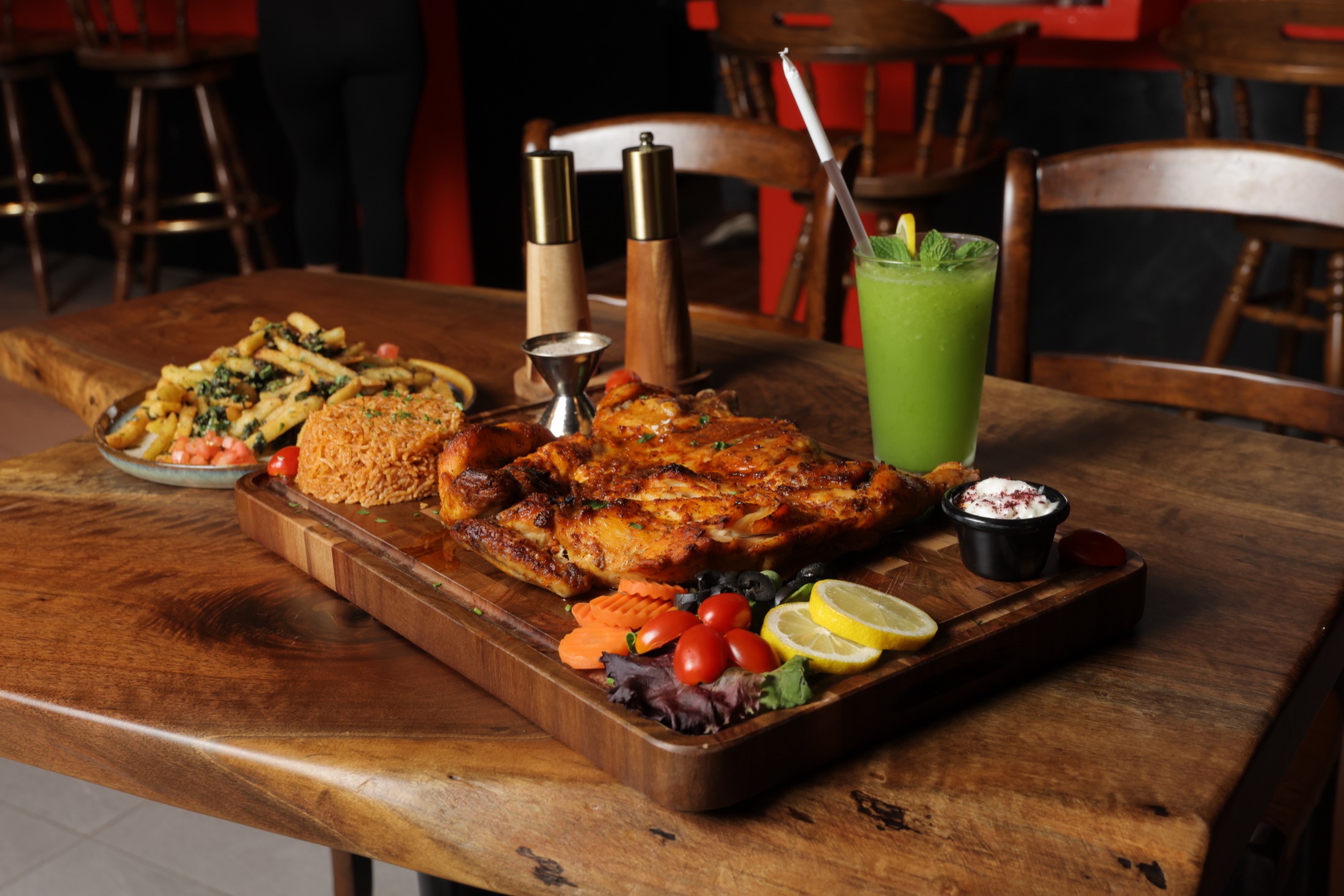 A grilled chicken platter on a live-edge walnut table inside Rooh's dining room, flame-red chairs behind